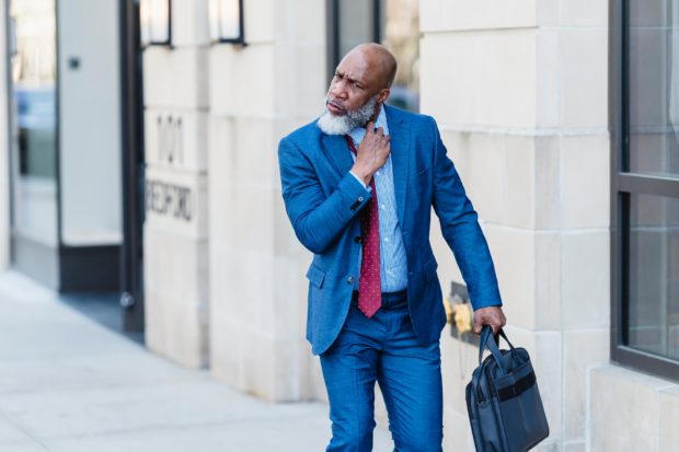 Older Black man in a suit, loosening his tie as he leaves work on a city street. The concept of quiet quitting.