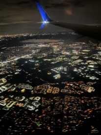 The night sky and city lights below from an airplane window.