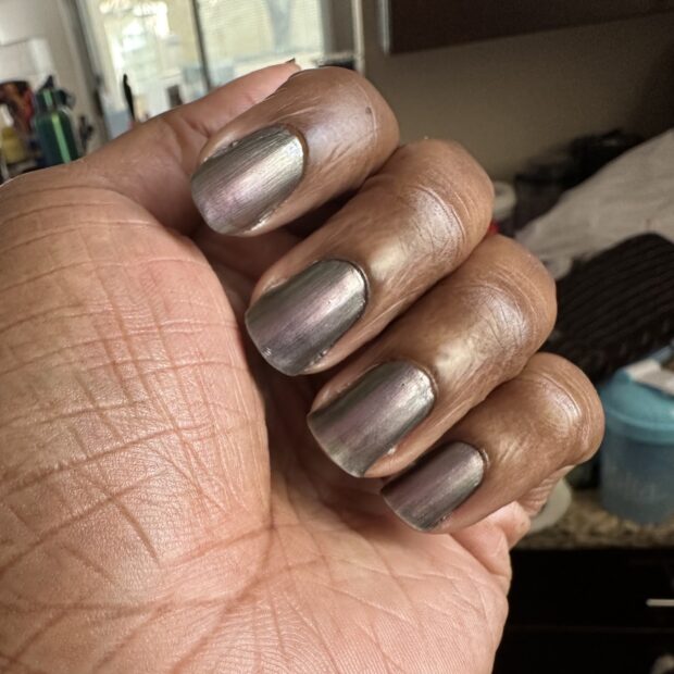 Fingers of a hand curled over to show the fingernails, painted with a purple-grey nail polish.